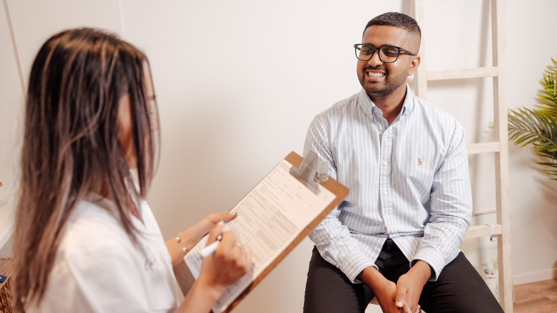 Image of man smiling at pharmacist who's taking notes on clipboard