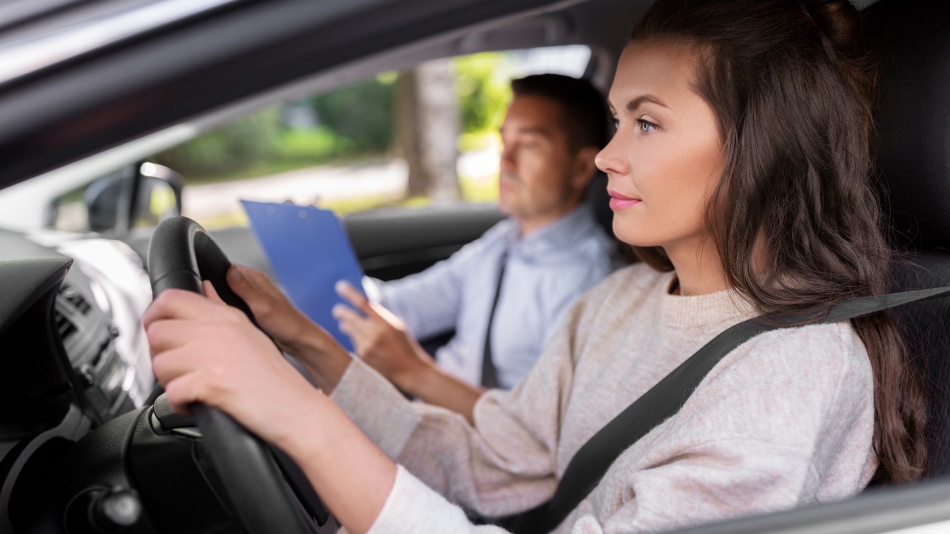 Image of woman driving with examiner holding clipboard in passenger's seat